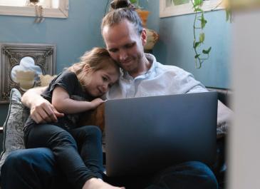 Father with daughter on his knee looking at laptop screen