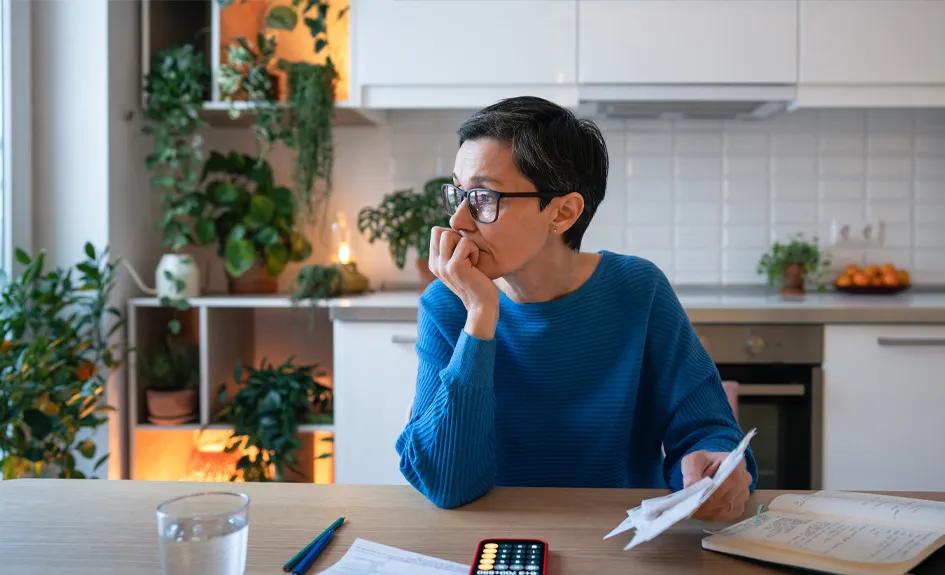 Worried woman with bills and calculator, sitting at kitchen table.