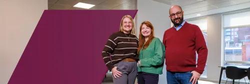 Three coworkers standing in a row by spotlight