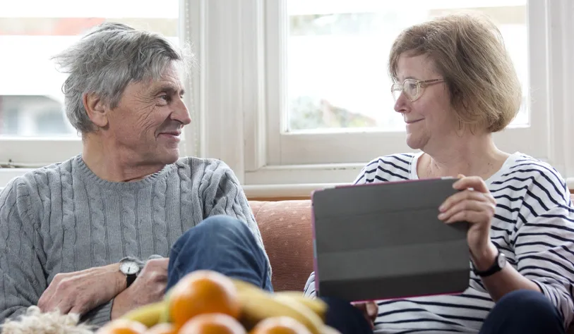 A man and woman smile at each other while holding an iPad