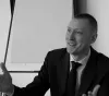 Jamie Bell is wearing a suit, gesturing during a discussion in front of a blank flip chart